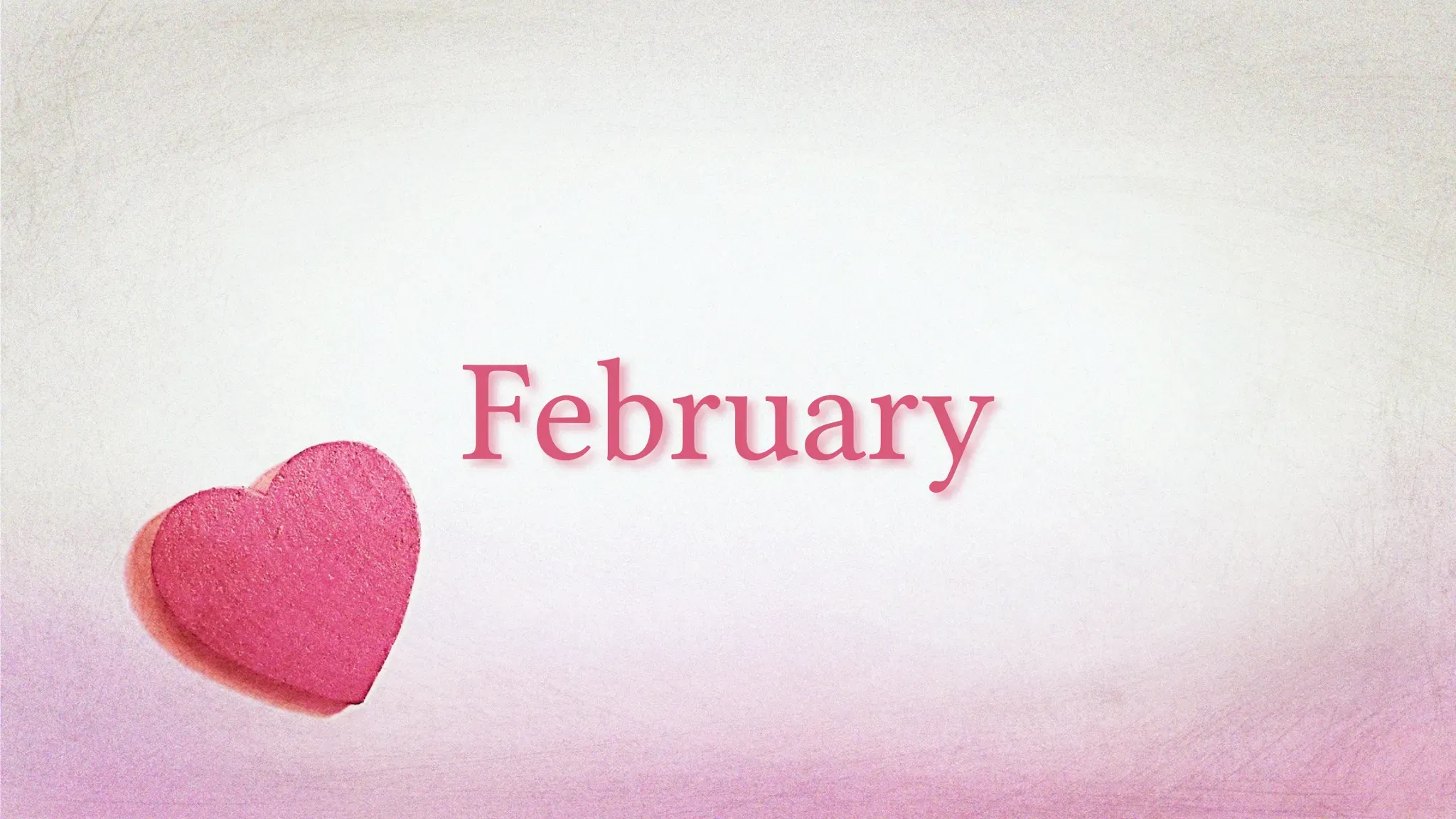 The word "February" in pink serif text on a light textured background with a pink conversation heart in the lower left corner