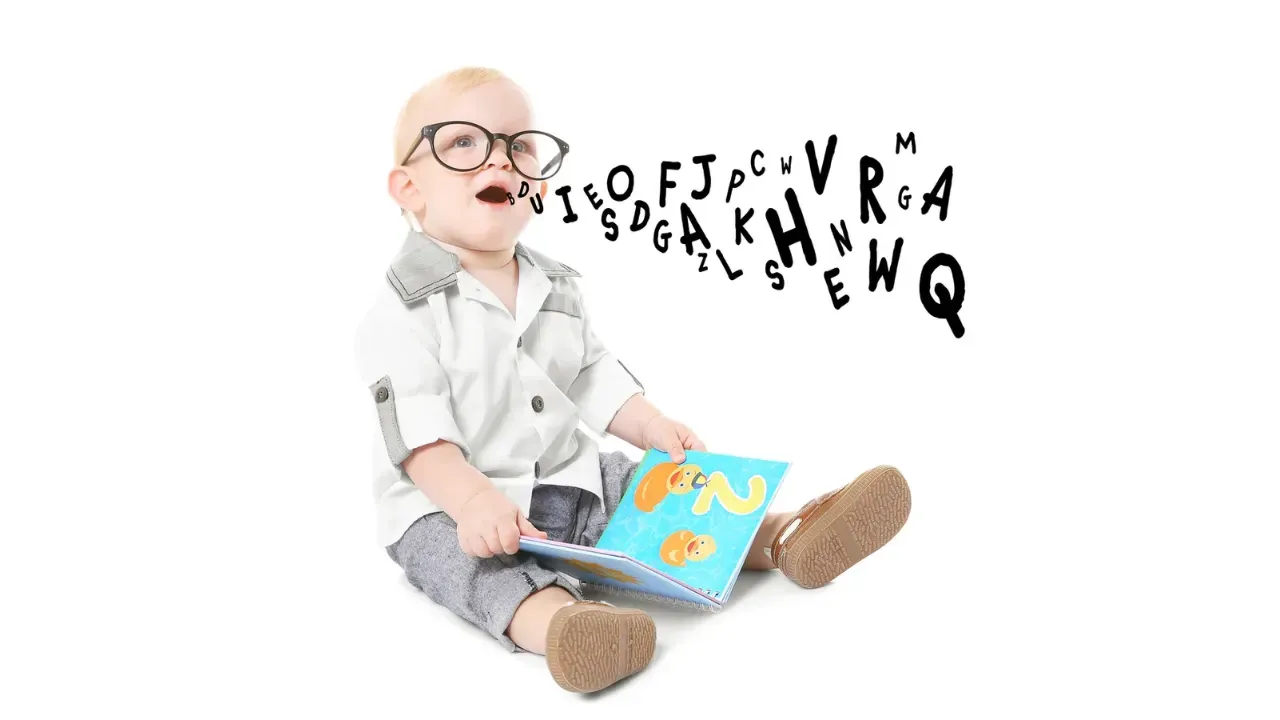 A baby wearing glasses sits holding a colorful book, with scattered alphabet letters floating around their head